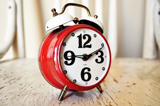 Close-up of vintage red alarm clock on rustic wood surface, indoors.